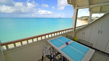 A balcony with a table and chairs, overlooking a beach and the ocean.