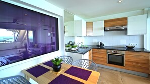 A modern kitchen with wooden cabinets, a stainless steel oven, and a dining area with purple placemats and a potted plant. - Grand Case beach (Grand Case)