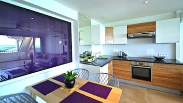 A modern kitchen with wooden cabinets, a stainless steel oven, and a dining area with purple placemats and a potted plant.