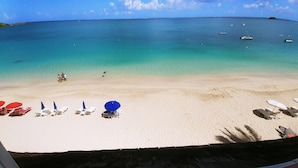 A beach with clear turquoise water, a sandy shore, and several sun loungers with umbrellas. - Grand Case beach (Grand Case)