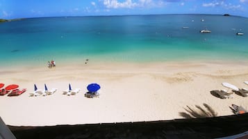 A beach with clear turquoise water, several boats, and sun loungers with umbrellas.