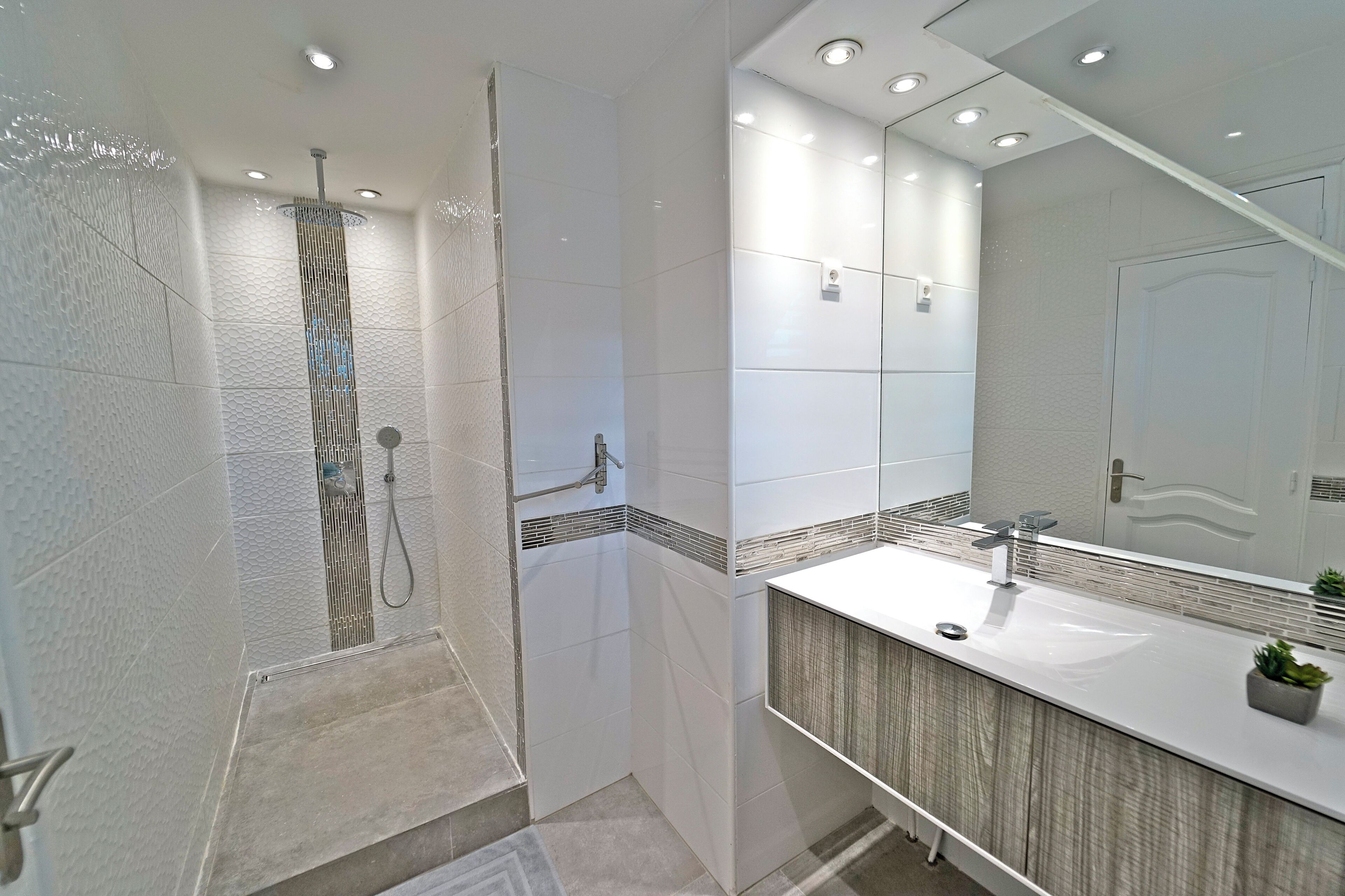 A modern bathroom with a walk-in shower, a large mirror, and a wooden vanity.
