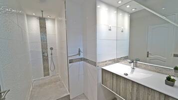A modern bathroom with a walk-in shower, a large mirror, and a wooden vanity.