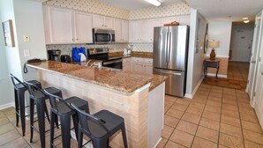 Una cocina con armarios blancos, encimera de granito, refrigerador de acero inoxidable y cafetera.