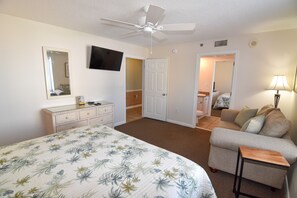 Ein Schlafzimmer mit einem Bett, einem Schminktisch, einem Deckenventilator, einem Fernseher, einer Couch und einer Lampe.