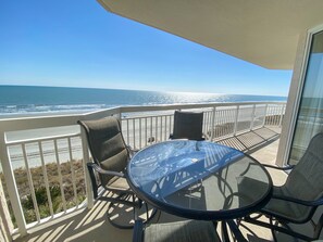Ein Balkon mit Glastisch und Stühlen, der Blick auf einen Strand und den Ozean freigibt.