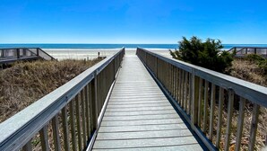 Un paseo marítimo de madera que conduce a una playa con cielos despejados.