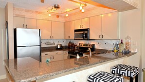 A modern kitchen with granite countertops, stainless steel appliances, and bar stools. - Gulf View, Steps from the Beach, Family Friendly (Destin)