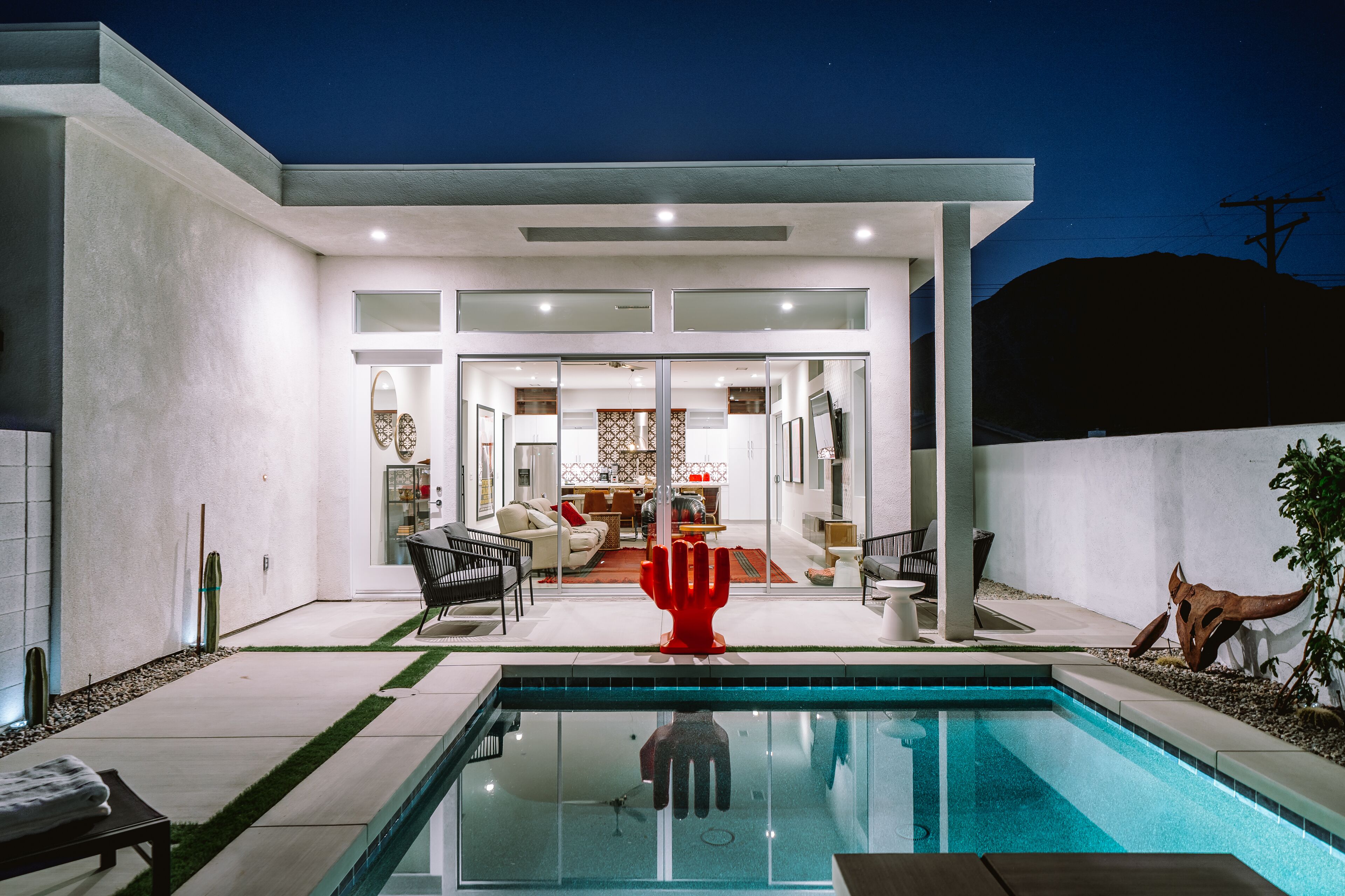 A modern house with a swimming pool, a red hand sculpture, and a patio area.