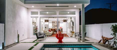 A modern house with a swimming pool, a red hand sculpture, and a patio area.
