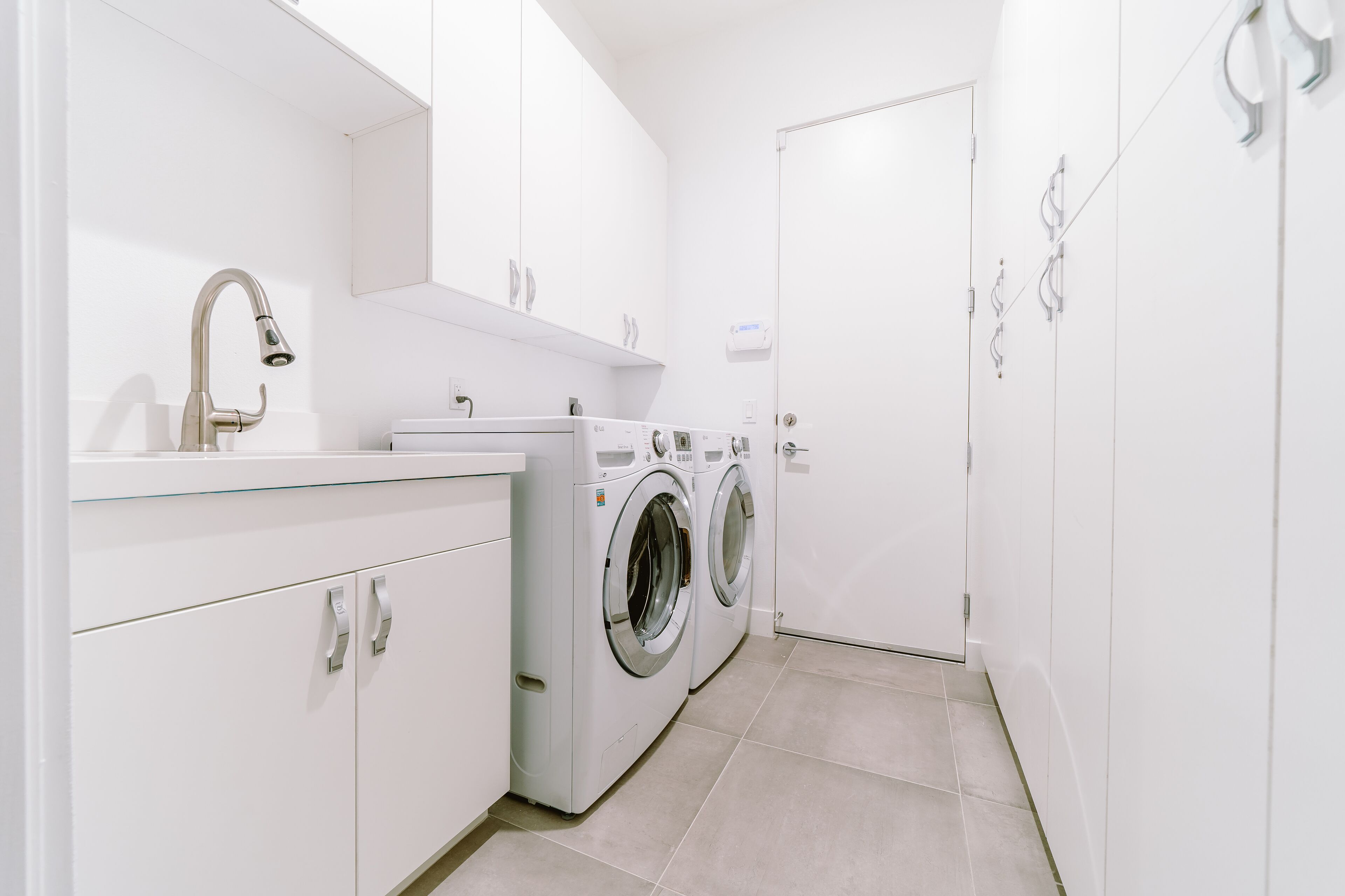 A modern, white-walled laundry room with a stainless steel faucet, a washing machine, and a dryer.