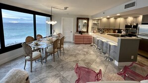 Une cuisine moderne avec vue sur l’océan, comprenant un coin repas avec une table et des chaises en verre, un bar et des appareils électroménagers contemporains.