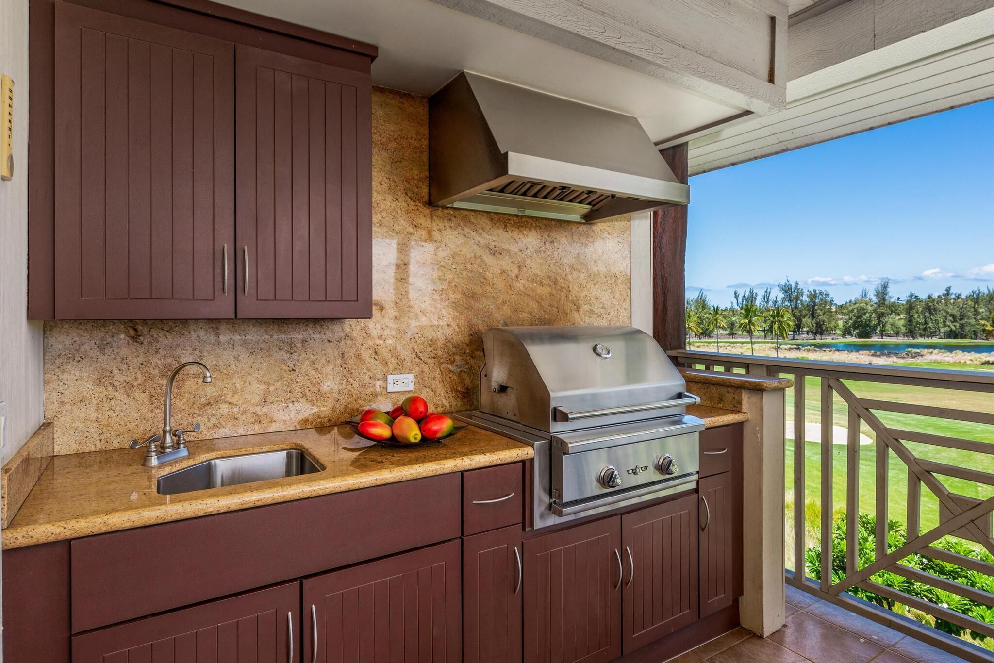Una cocina con encimeras de granito, un lavamanos de acero inoxidable, una parrilla empotrada y vistas a un campo de golf.