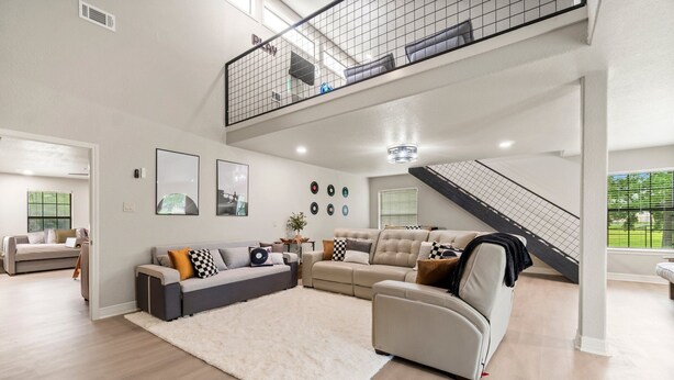 Un salón amplio con un sofá modular grande, un manto mullido blanco y una escalera que conduce a un nivel superior.