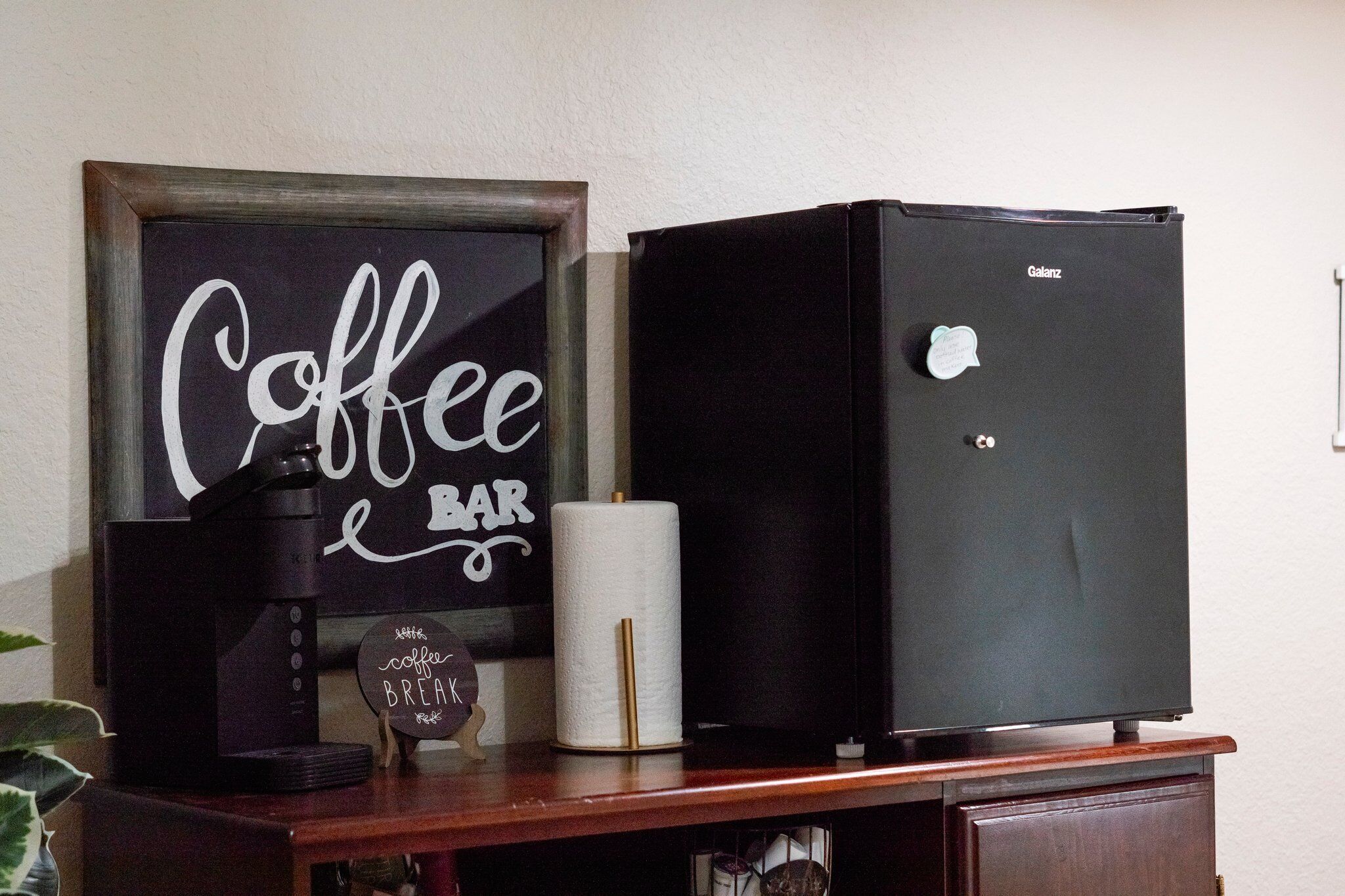 Una barra de café con una máquina de café, un letrero que dice "Coffee Bar" y un refrigerador negro con una etiqueta.
