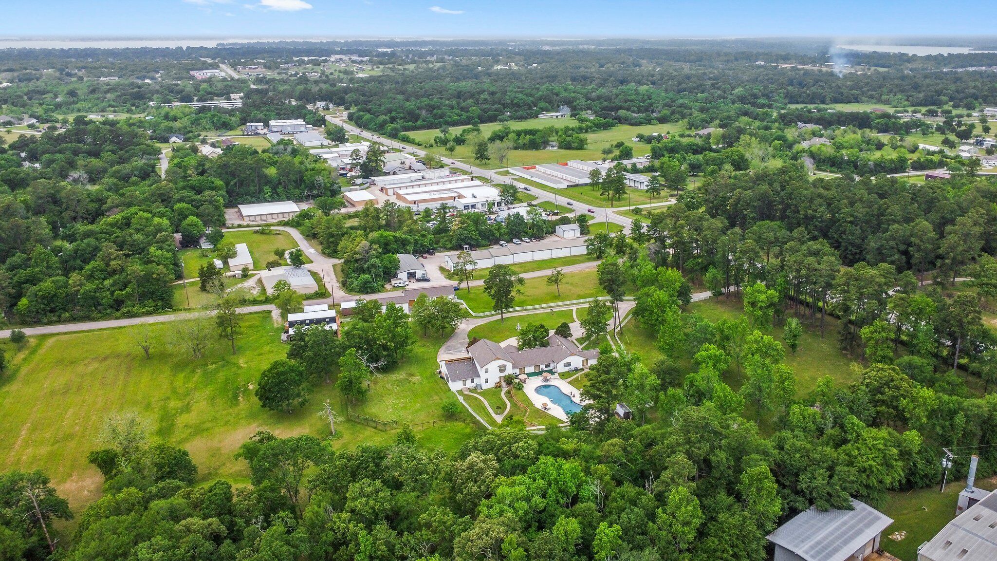 An aerial view of a residential area with multiple houses, a swimming pool, and surrounding greenery.
