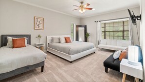 Une chambre moderne avec deux lits, un ventilateur de plafond, une grande fenêtre avec stores et une lampe de chevet.