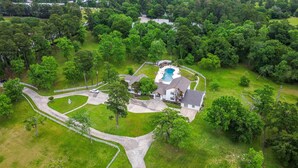 Vista aérea de una propiedad residencial con piscina, entrada para vehículos y vegetación circundante.