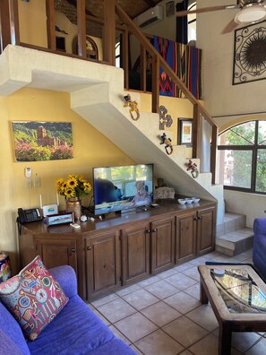 A living room with a TV, a sofa, a coffee table, and a staircase.