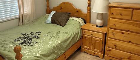 A bedroom with a wooden bed, a nightstand with a lamp, a dresser, and a framed picture on the wall.