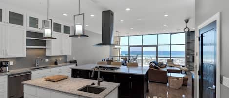 A modern kitchen with a large island, white cabinetry, and a view of the ocean.