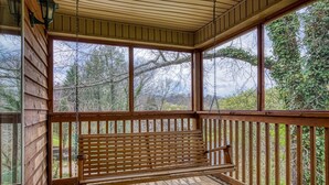 A wooden deck with a bench, large windows, and a view of trees. - River View Rental-Gameroom-Only 1 Mile Off Main Parkway Pigeon Forge-Hot Tub and more (PIGEON FORGE)