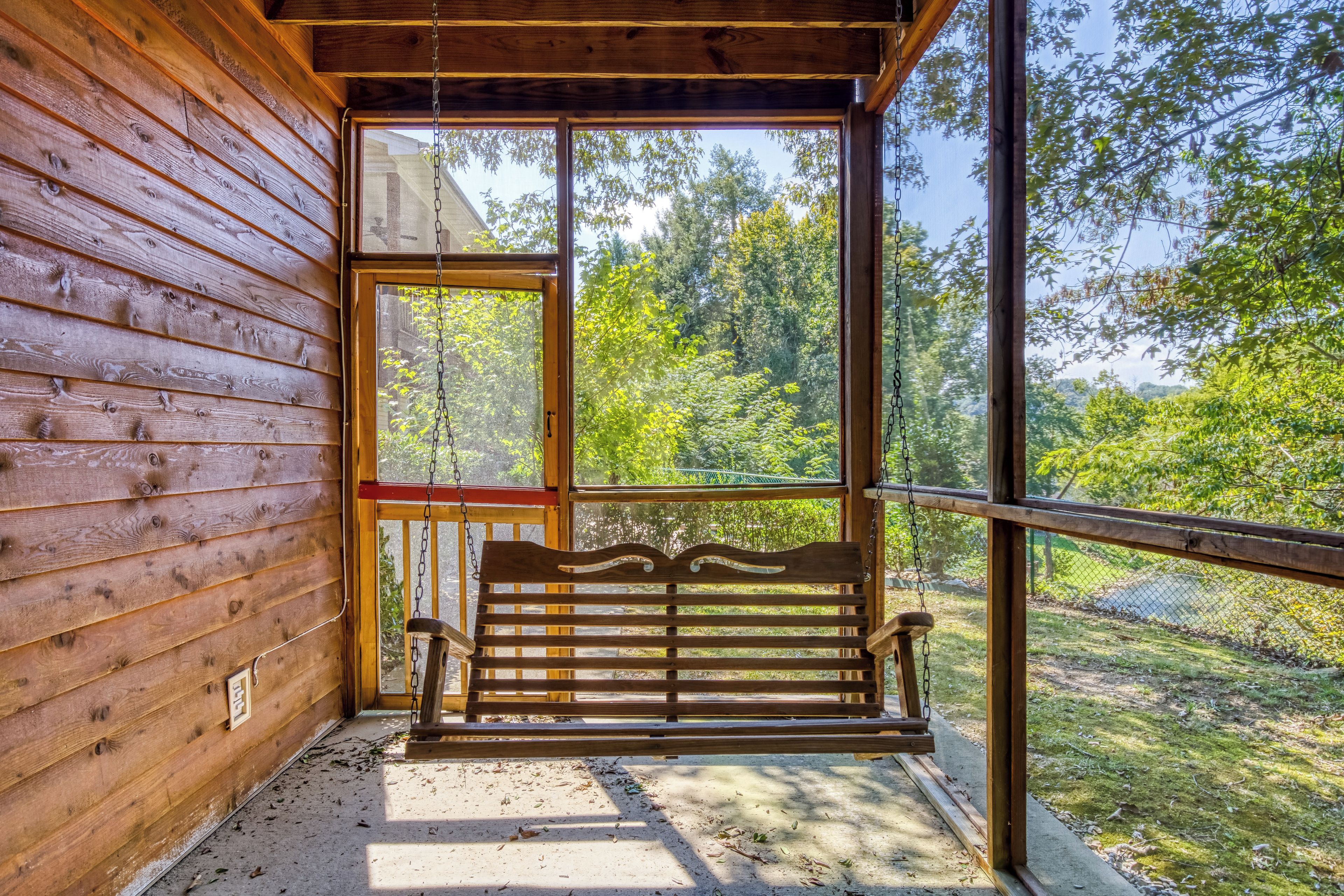 A wooden cabin with a bench outside a large window overlooking a forest.