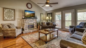A living room with a stone fireplace, patterned armchairs, a coffee table, and a ceiling fan. - River View Rental-Gameroom-Only 1 Mile Off Main Parkway Pigeon Forge-Hot Tub and more (PIGEON FORGE)