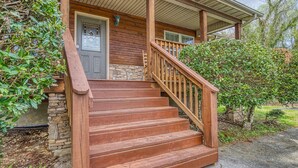 A wooden staircase leading to a front door with a stone base, surrounded by greenery. - River View Rental-Gameroom-Only 1 Mile Off Main Parkway Pigeon Forge-Hot Tub and more (PIGEON FORGE)