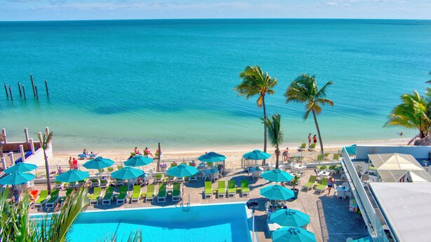 A beach resort with a pool, lounge chairs, umbrellas, and palm trees. - Lazy Tortuga ground level 2bed/2bath half duplex with dockage & cabana club (Key Colony)