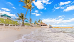 A beach with lounge chairs, palm trees, and a thatched-roof structure. - Lazy Tortuga ground level 2bed/2bath half duplex with dockage & cabana club (Key Colony)