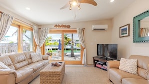 A living room with a sofa, a TV, a woven coffee table, and a ceiling fan. - Lazy Tortuga ground level 2bed/2bath half duplex with dockage & cabana club (Key Colony)