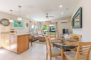 A modern kitchen with a central island, a dining area with a glass table, and a view of a pool and outdoor seating.