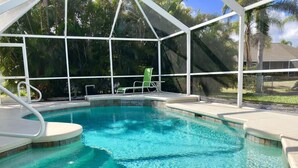 Une piscine d’un bleu éclatant, bordée d’une terrasse blanche et dotée d’un espace abrité avec des chaises.