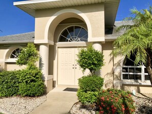 A house with a beige facade, a white door, and a small porch with a window. - Prime location overlooking canal! (Cape Coral)