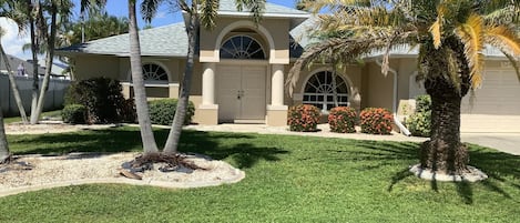 A residential house with a well-maintained lawn, palm trees, and a garage.