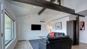 Ein modernes Wohnzimmer mit einer schwarzen Ledersofa, einem flachbildfernseher an der Wand und einem Holzbalken an der Decke.