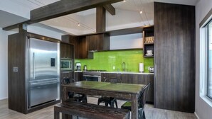 Eine moderne Küche mit einem Edelstahlkühlschrank, einer grünen Spritzschutzwand und Holzschränken.