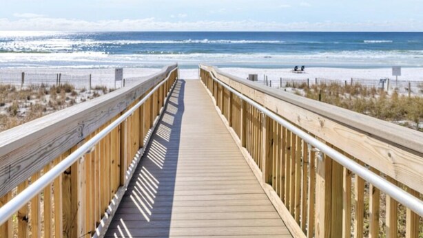 A wooden boardwalk leading to a beach with a clear view of the ocean.