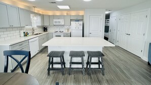 A modern kitchen with white cabinets, a large island, and three stools.