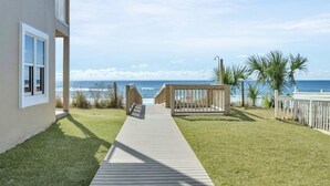 A wooden pathway leading to a beach view, with a building on the left and palm trees on the right.