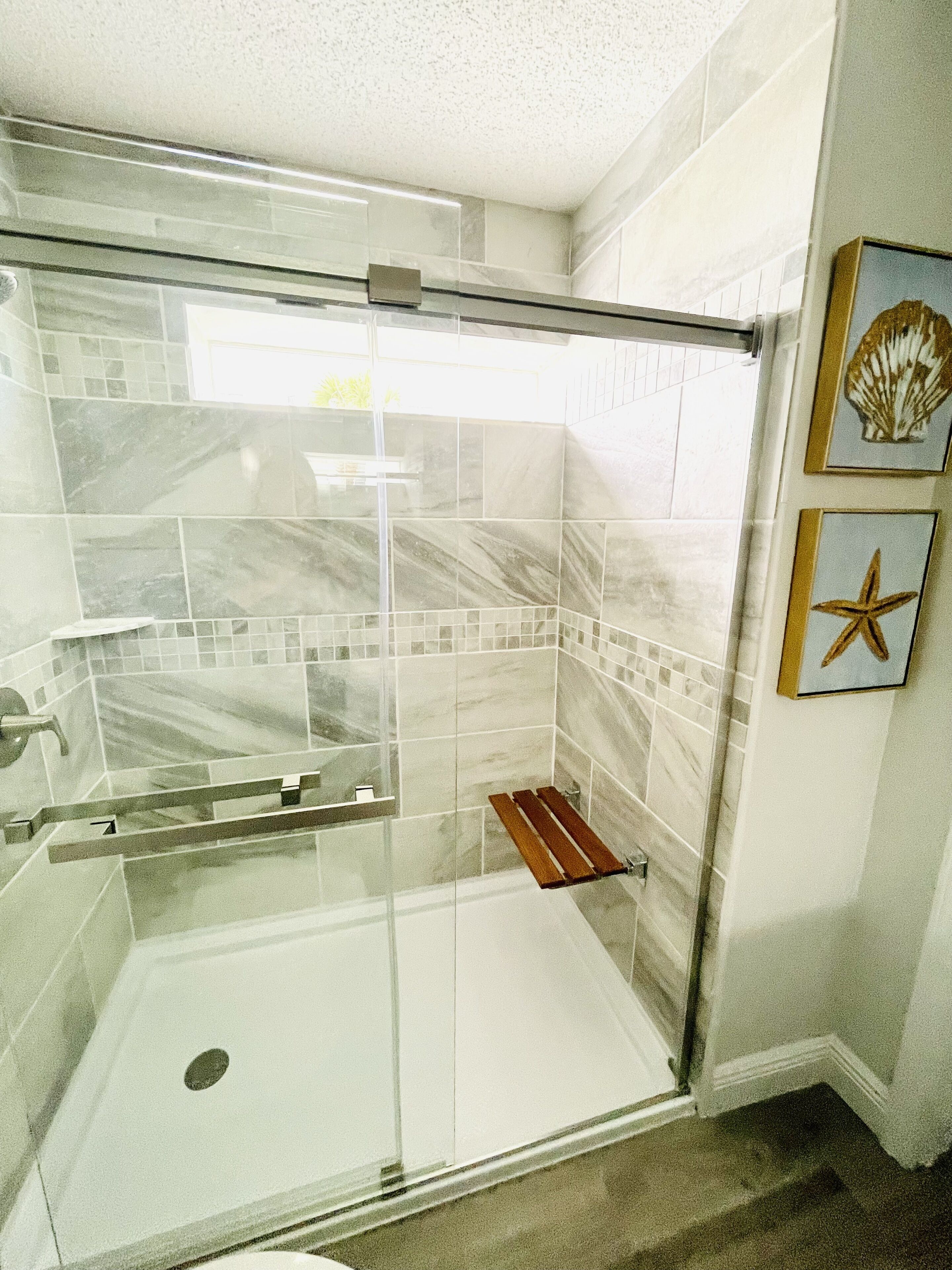 Une salle de bain moderne avec une douche à parois de verre, des murs carrelés et une étagère en bois.
