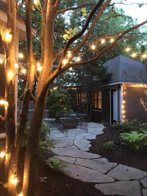 A stone pathway leading to a house with string lights and a tree in the foreground. - ALL 5 STAR REVIEWS! Walk to lake, dining & coffee. Private hot tub, assoc pool. (Union Pier)