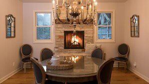 A dining room with a stone fireplace, a chandelier, and a round table with chairs. - ALL 5 STAR REVIEWS! Walk to lake, dining & coffee. Private hot tub, assoc pool. (Union Pier)