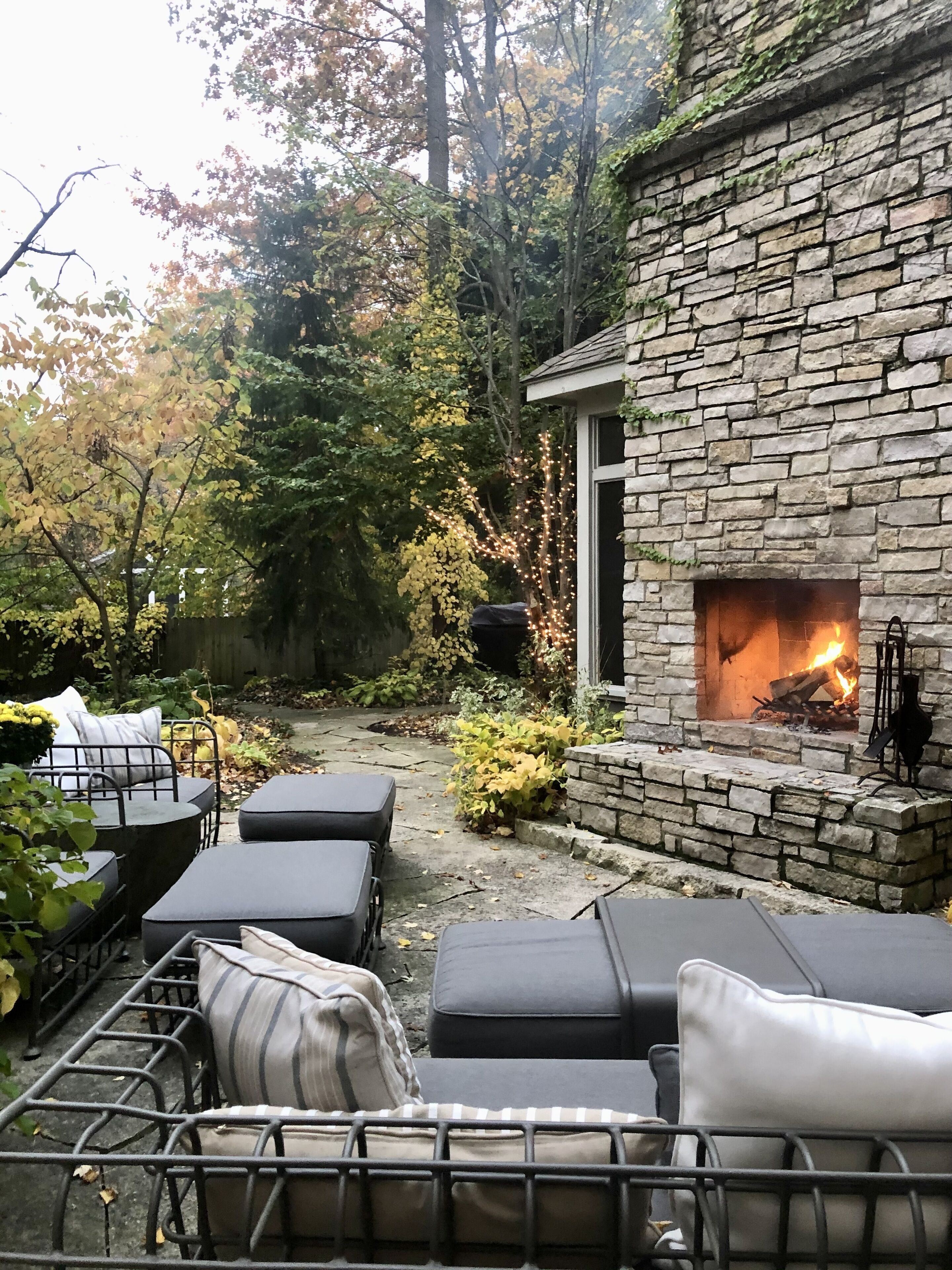 A stone fireplace with a fire, surrounded by outdoor seating with cushions.