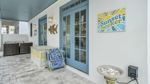 A covered patio area with a blue door, wicker furniture, a small table, and a decorative sign. - Sunset Seeker-Gulf Side 30A Villa w/ Community Pool,Pet Friendly! (Seacrest Beach)