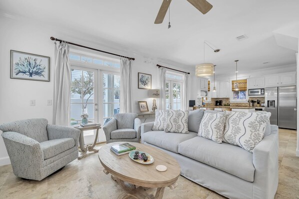A living room with a sofa, two armchairs, a coffee table, and a kitchen in the background.