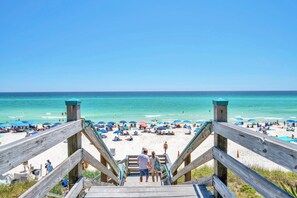 A wooden staircase leading to a beach with umbrellas and people.