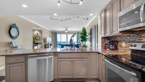Une cuisine moderne dotée d’un îlot central, d’appareils électroménagers en acier inoxydable et offrant une vue sur l’extérieur.