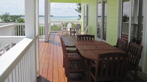 A covered porch with a wooden table and chairs, overlooking a beach. - PRIVATE LUXURY Beachfront Home, Beach Cabana, Kayaks, Paddle Board (Casuarina Point)